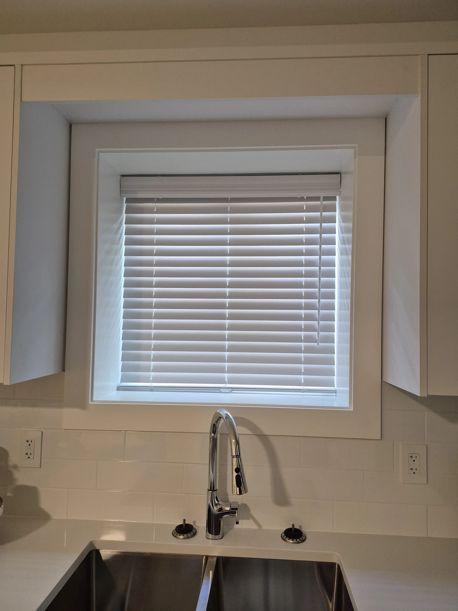 White horizontal blinds within the kitchen window above a stainless-steel sink