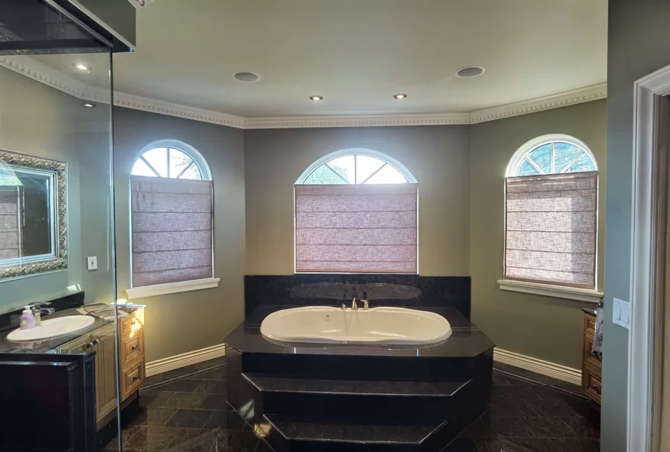Three Roman shades covering rectangular window sections below uncovered arched tops in a bathroom