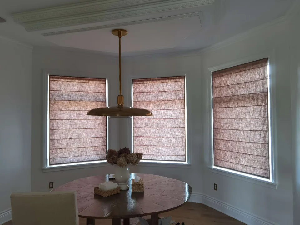 Three fabric Roman shades follow the dining bay, with daylight filtering through the textured material