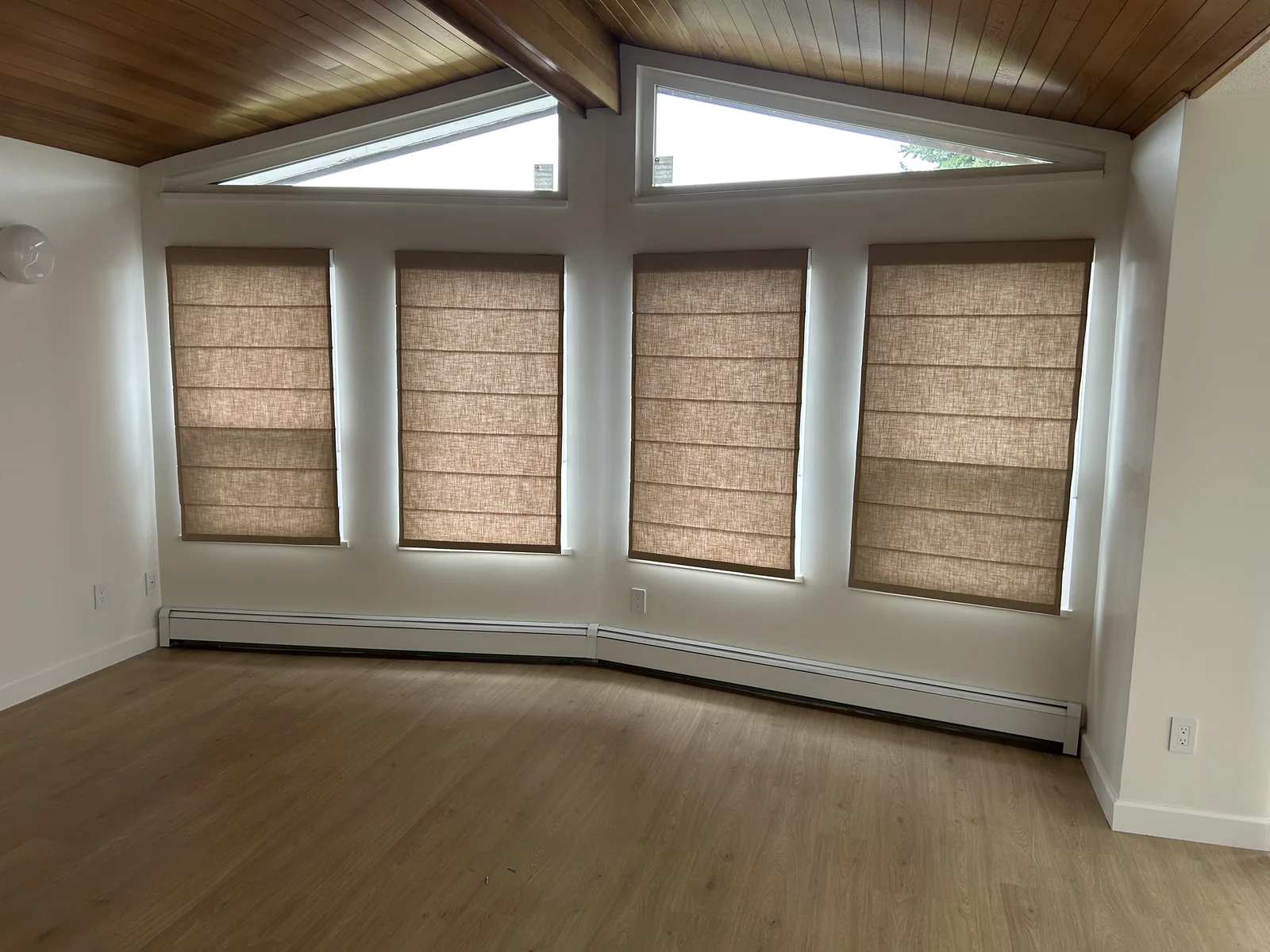 Four textured Roman shades at a curved window wall below triangular upper glazing and a timber ceiling