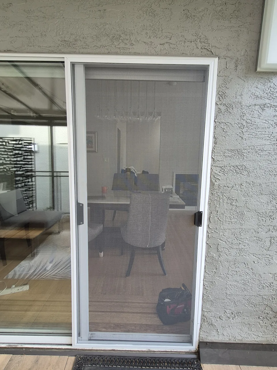 White-framed sliding mesh screen door viewed from the patio, with a dining table and chairs visible through the mesh