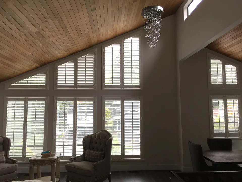 Shaped shutter panels follow the angled upper windows beneath a timber ceiling, coordinated with rectangular shutters below