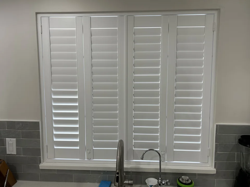 Four white shutter panels sit within the kitchen window above the sink, with the louvres shown in a mostly closed position