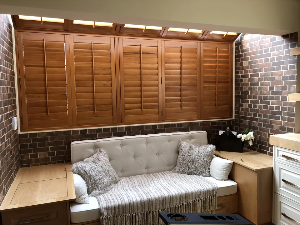 Wood-toned shutters span the window behind the sofa, creating a warm backdrop against exposed brick