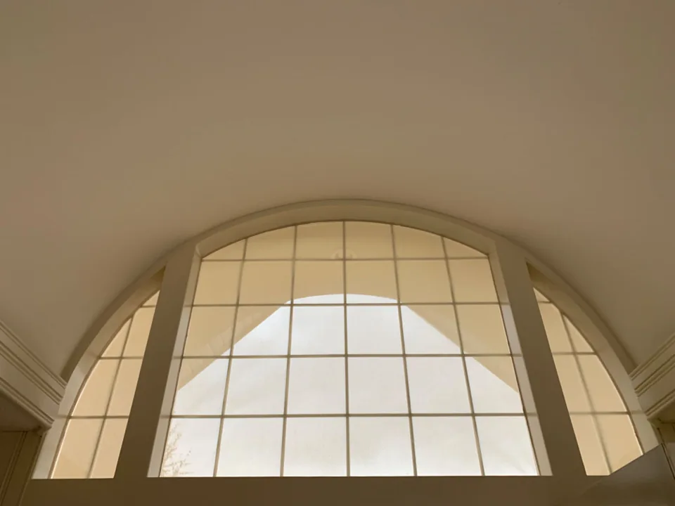 A shaped treatment follows the outline of a broad arched window with divided glazing