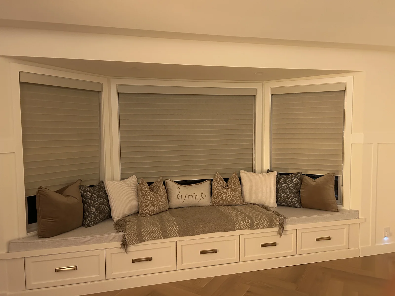 Warm neutral Vienna shades following three bay windows above a white cushioned window seat