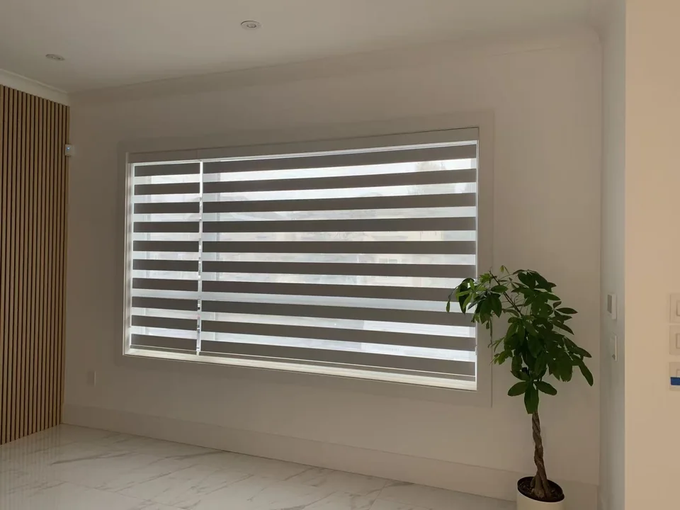 Alternating sheer and opaque bands sit within a pale window recess, with a plant beside the opening