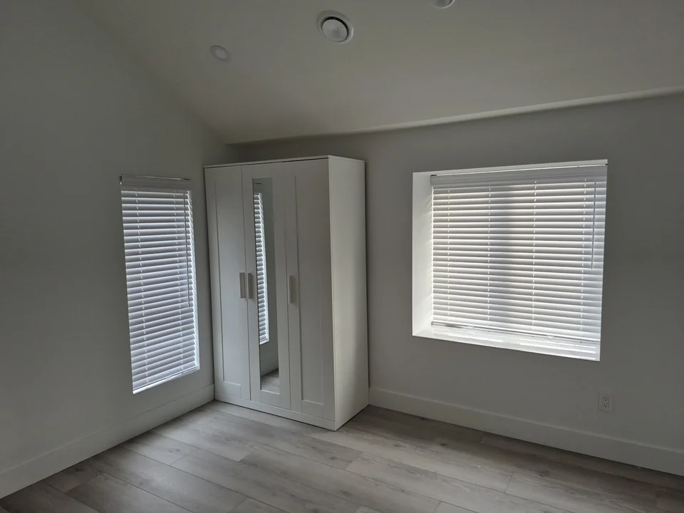 Matching white faux wood blinds on two different-sized windows beside a white wardrobe